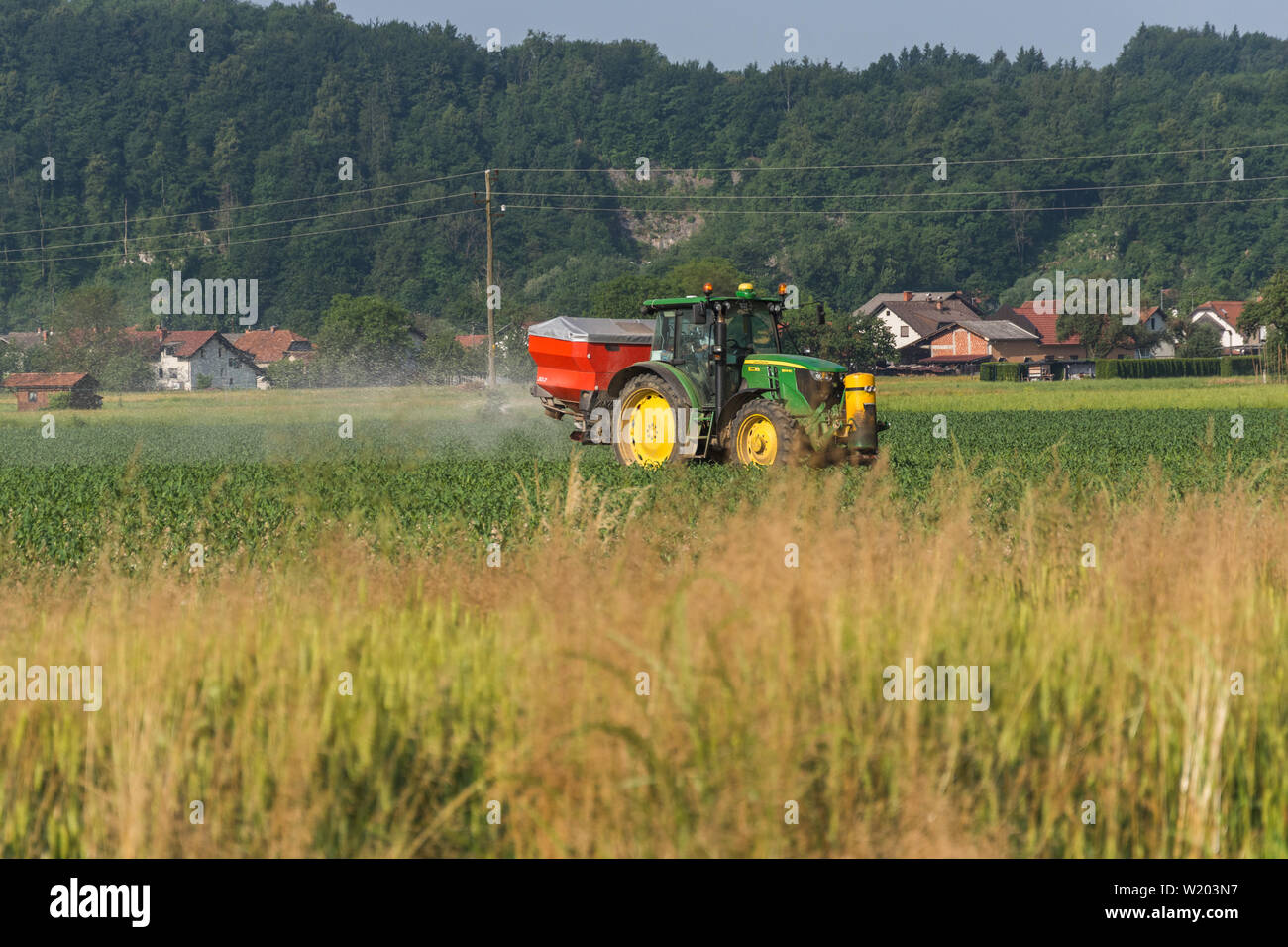 John Deere tractor with red tank in the back spraying on a field Stock Photo