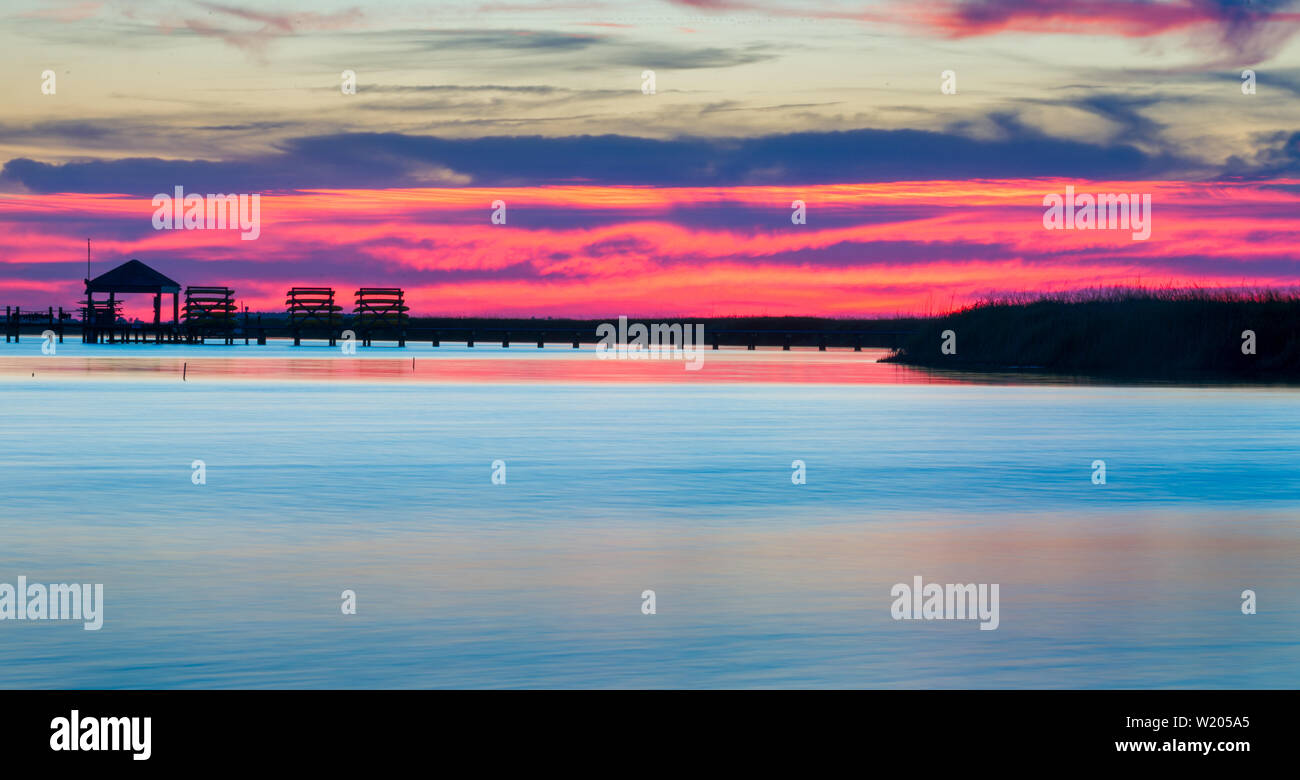 Sunset Outer Banks North Carolina - Just after sun has crossed horizon on a cloudy day. Marsh and wetlands with gazebo on dock in distance. Stock Photo