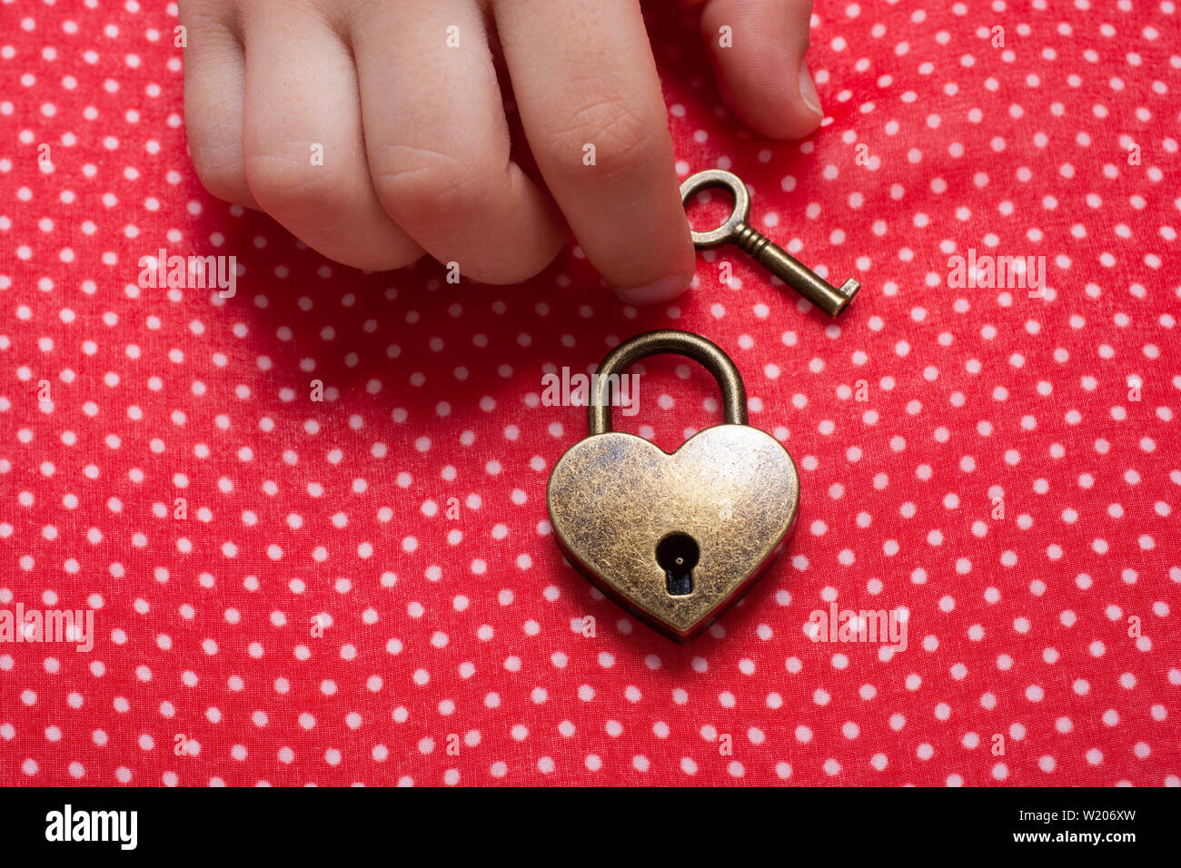 Hand holding a heart shaped lock and key on a red background Stock ...