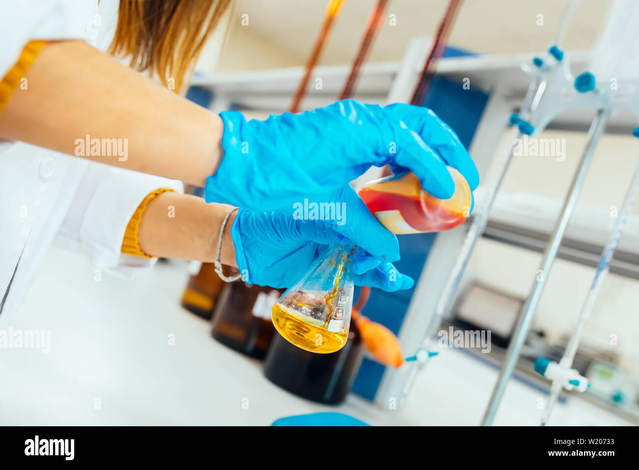 Woman or female hands in protective gloves hold test tube in hands produces chemistry experiment test and research in modern chemistry lab. Stock Photo