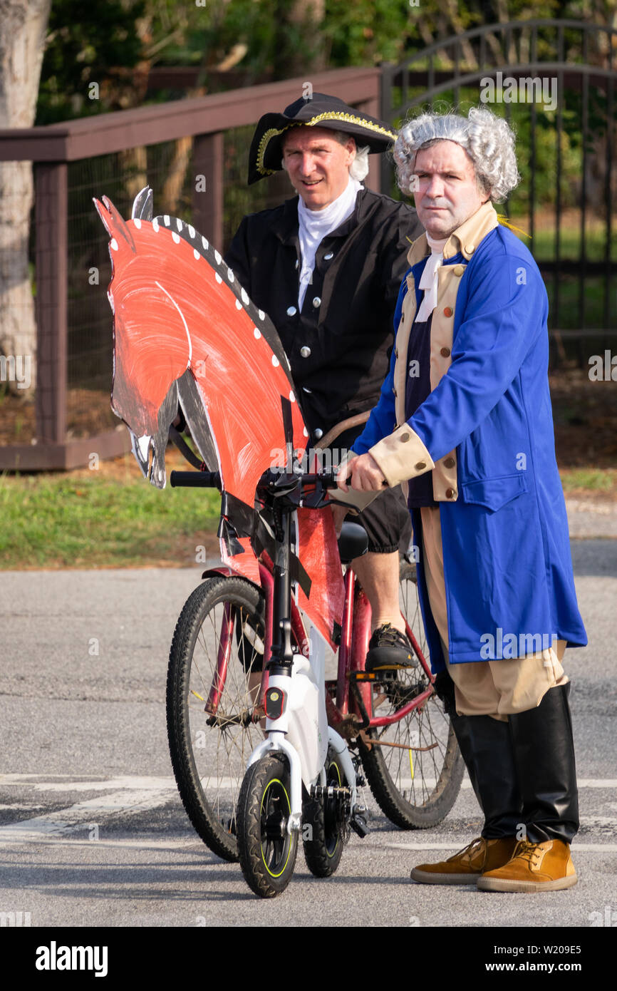 Sullivans Island South Carolina, USA. 4th July, 2019. Men dressed in colonial costumes of the founding fathers ride bicycles decorated as horses during the annual Independence Day parade July 4, 2019 in Sullivan's Island, South Carolina. The tiny Sea Island beach community across from Charleston, was once a quarantine station for enslaved Africans, and is now one of the most affluent, least diverse communities with one of highest per capita real estate costs in the United States. Credit: Planetpix/Alamy Live News Stock Photo