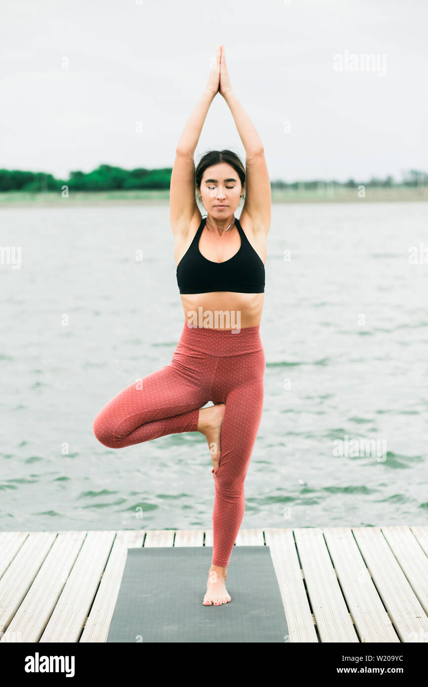 young asian girl doing yoga outdoors on the pier by the lake. she's wearing  a black top and red leggings Stock Photo - Alamy