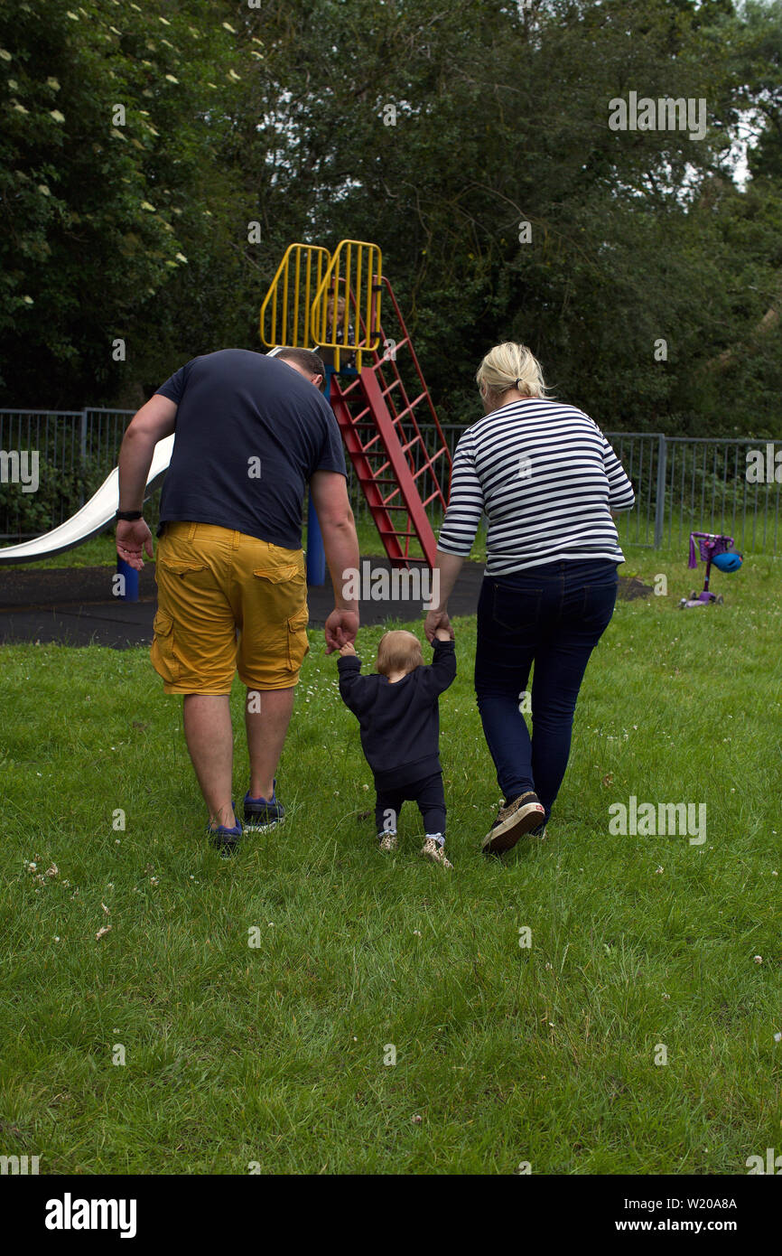 Toddler learning to walk in the park with parents Stock Photo