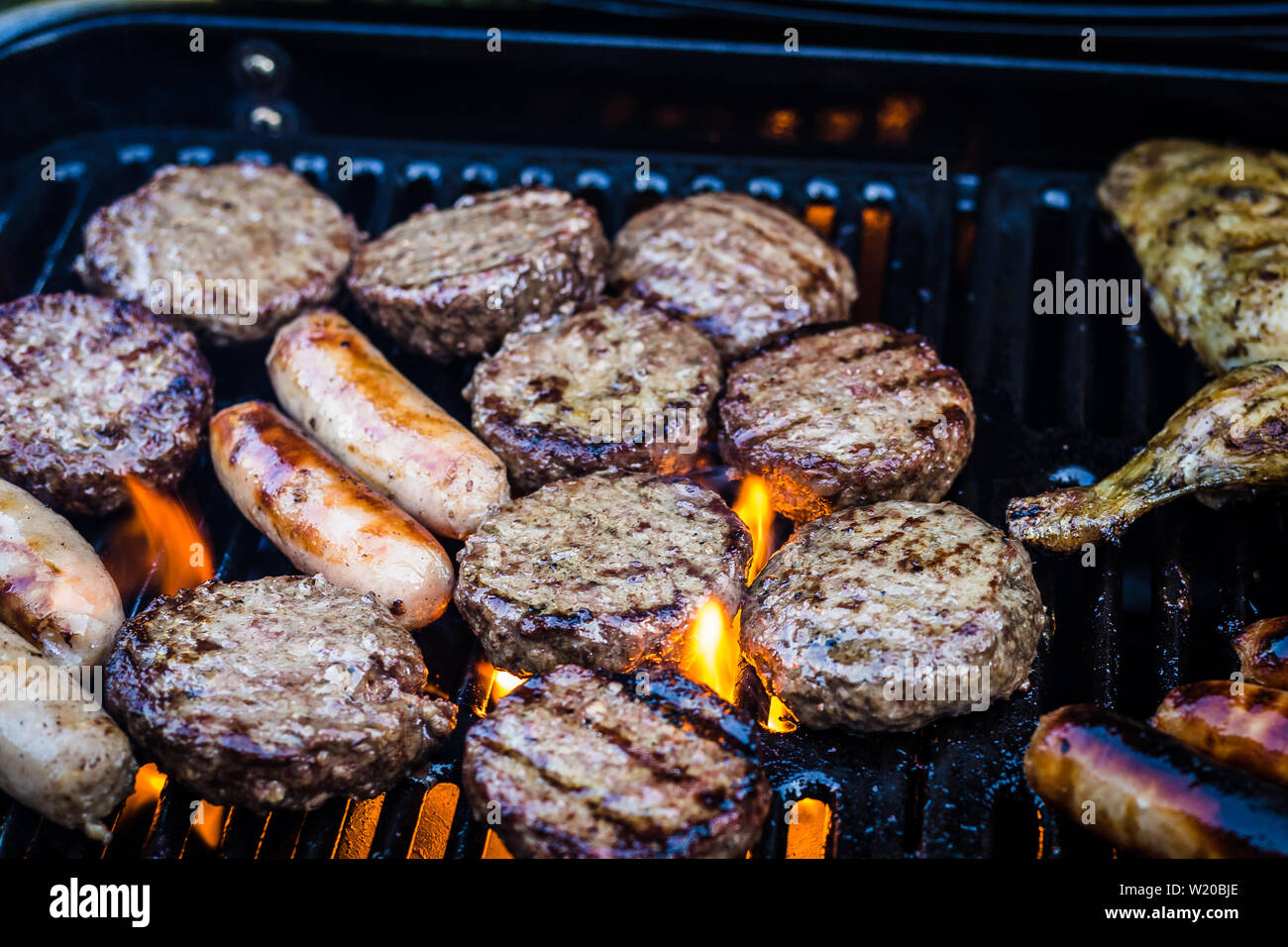 Burgers, Sausages and Chicken cooking. on a BBQ, Flames can be seen