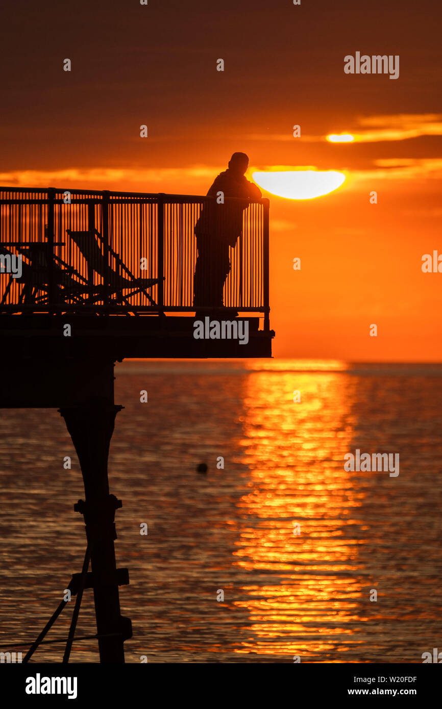 Aberystwyth Wales UK, Thursday 04 July 2019  UK Weather: People standing at the end of Aberystwyth’s truncated  seaside pier are silhouetted against the sky as they watch the glorious sunset in Aberystwyth on the Cardigan Bay coast, west Wales.   photo credit: Keith Morris//Alamy Live News Stock Photo