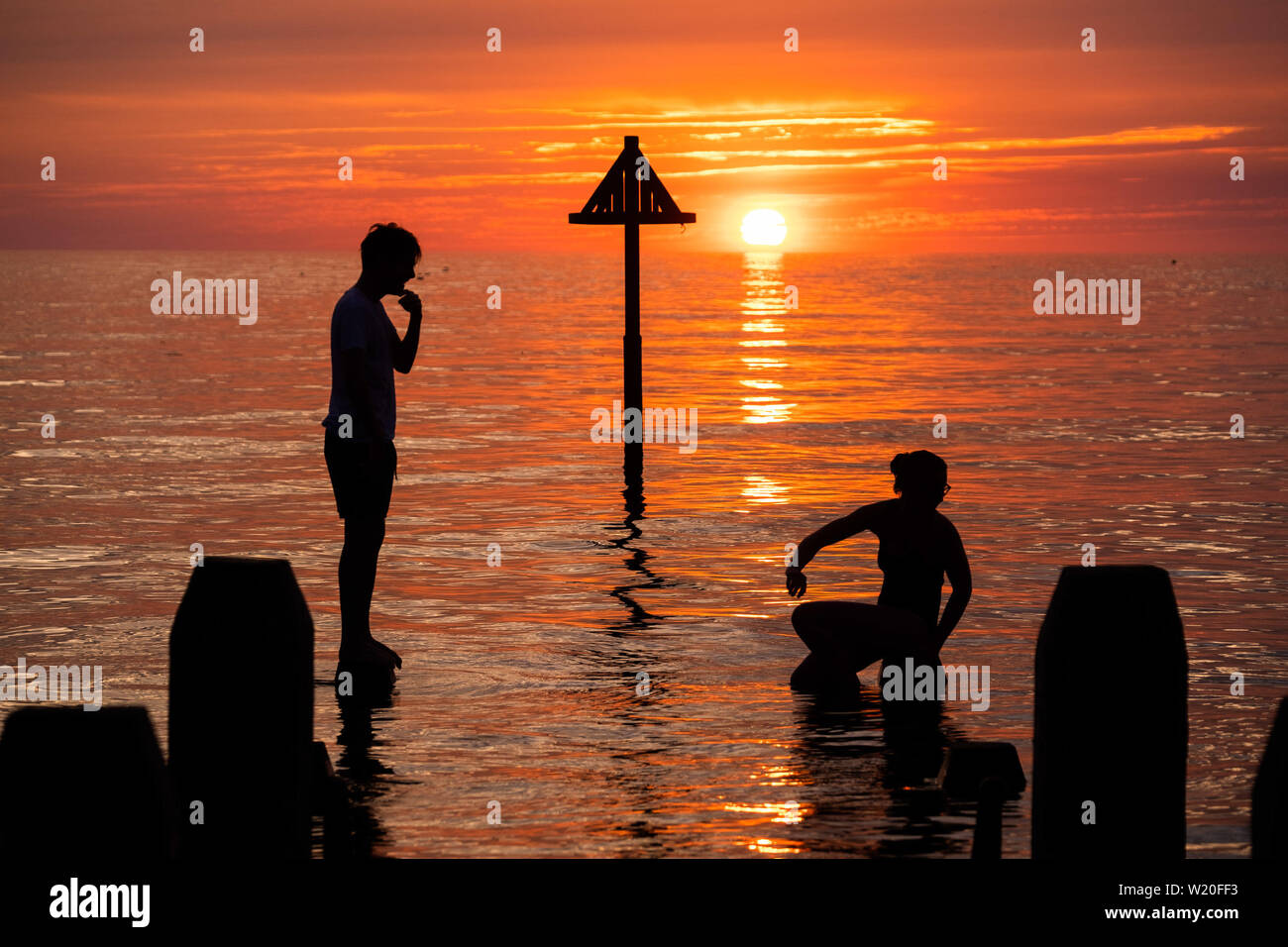 Aberystwyth Wales UK, Thursday 04 July 2019  UK Weather: A young couple are silhouetted against the sky as they balance on the wooden jetty  in the flat calm sea and watch the glorious sunset in Aberystwyth on the Cardigan Bay coast, west Wales.   photo credit: Keith Morris//Alamy Live News Stock Photo