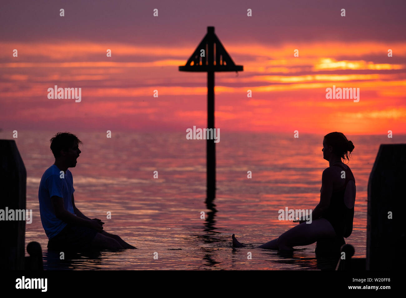 Aberystwyth Wales UK, Thursday 04 July 2019  UK Weather: A young couple are silhouetted against the sky as they balance on the wooden jetty  in the flat calm sea and watch the glorious sunset in Aberystwyth on the Cardigan Bay coast, west Wales.   photo credit: Keith Morris//Alamy Live News Stock Photo