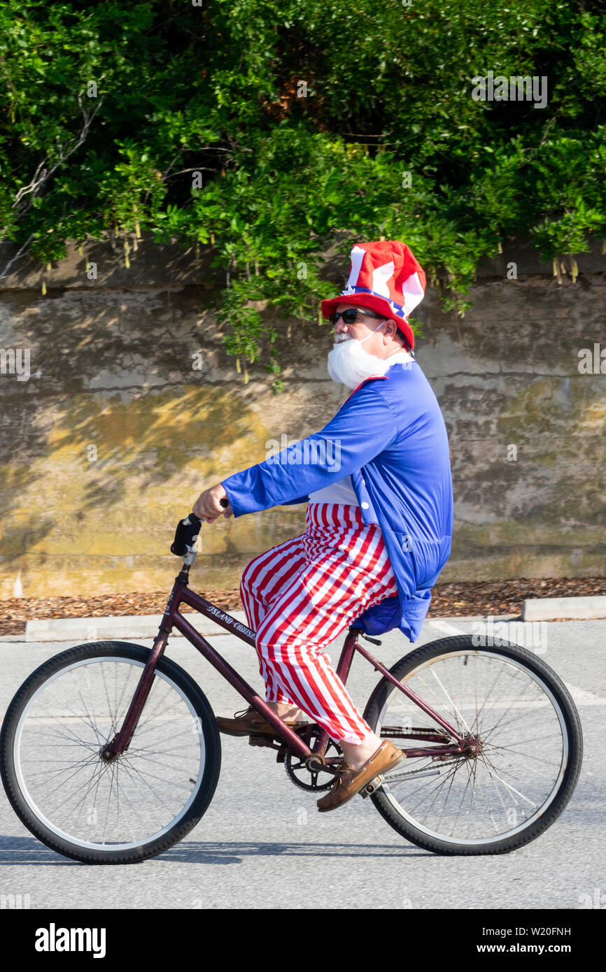 A man dressed in an Uncle Sam costume rides his bicycle in the annual Independence Day golf cart and bicycle parade July 4, 2019 in Sullivan's Island, South Carolina. The tiny affluent Sea Island beach community across from Charleston holds an outsized golf cart parade featuring more than 75 decorated carts. Stock Photo