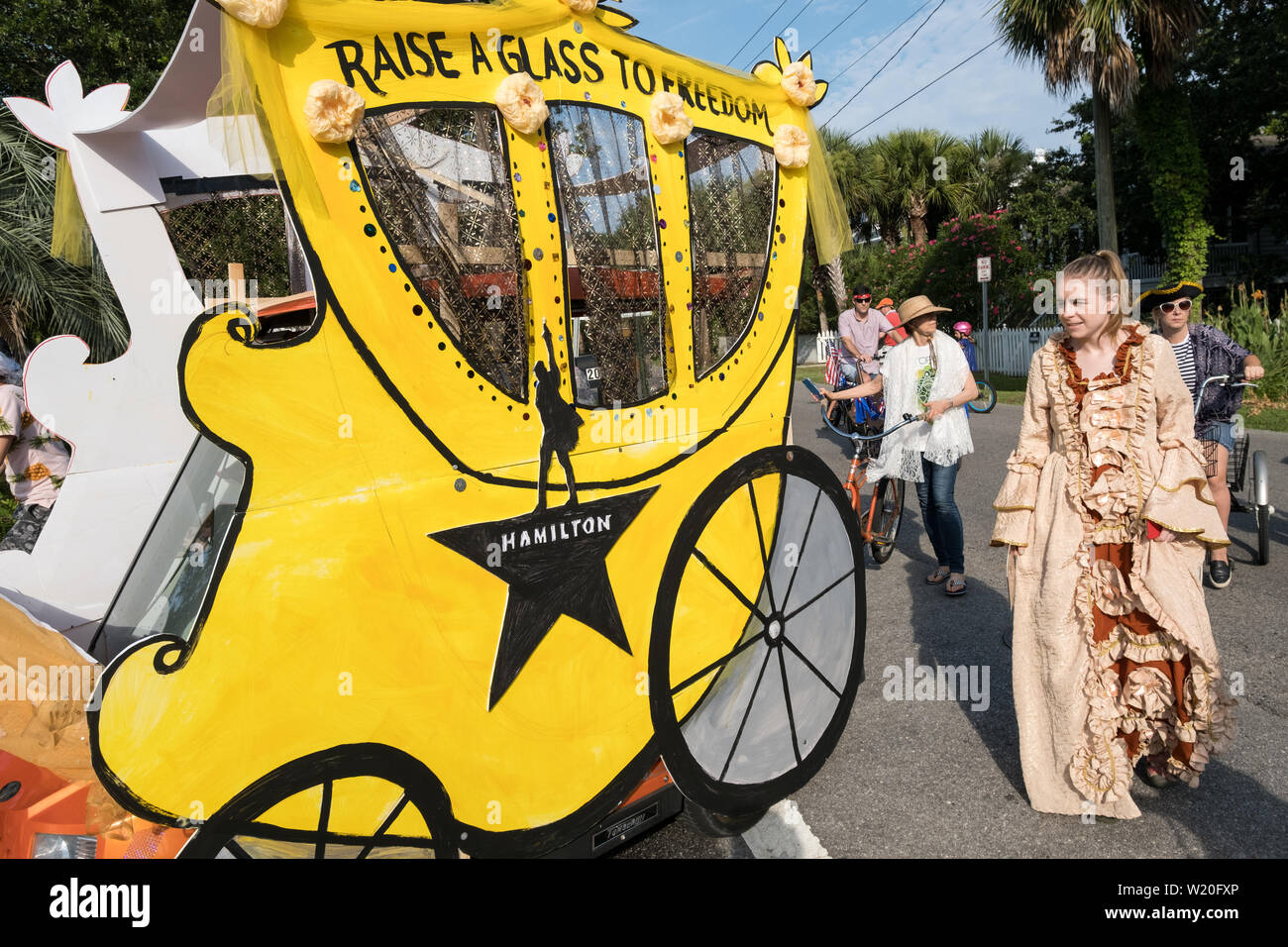 Women wearing colonial costume walk alongside a golf cart decorated as a horse carriage during the annual Independence Day parade July 4, 2019 in Sullivan's Island, South Carolina. The tiny affluent Sea Island beach community across from Charleston holds an outsized golf cart parade featuring more than 75 decorated carts. Stock Photo