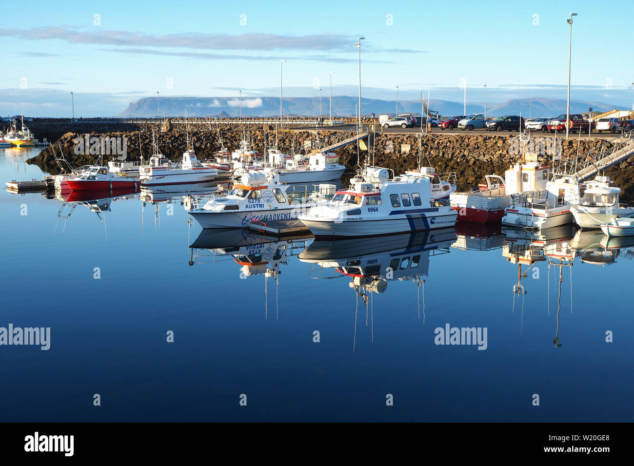 Boats moored in the harbour at Stykkisholmur, Iceland, with perfect reflections in the clear blue water, a blue sky and background mountains Stock Photo