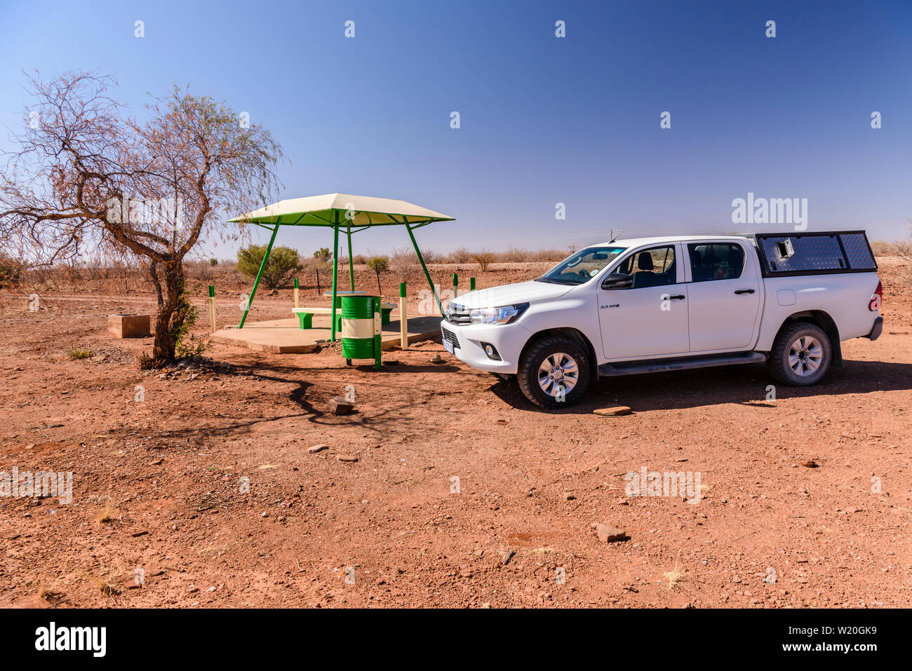 Toyota Hilux pick-up truck stopped beside a concrete picnic table and benches with a canopy for shade, typically placed every 10-20kms along roads in Stock Photo