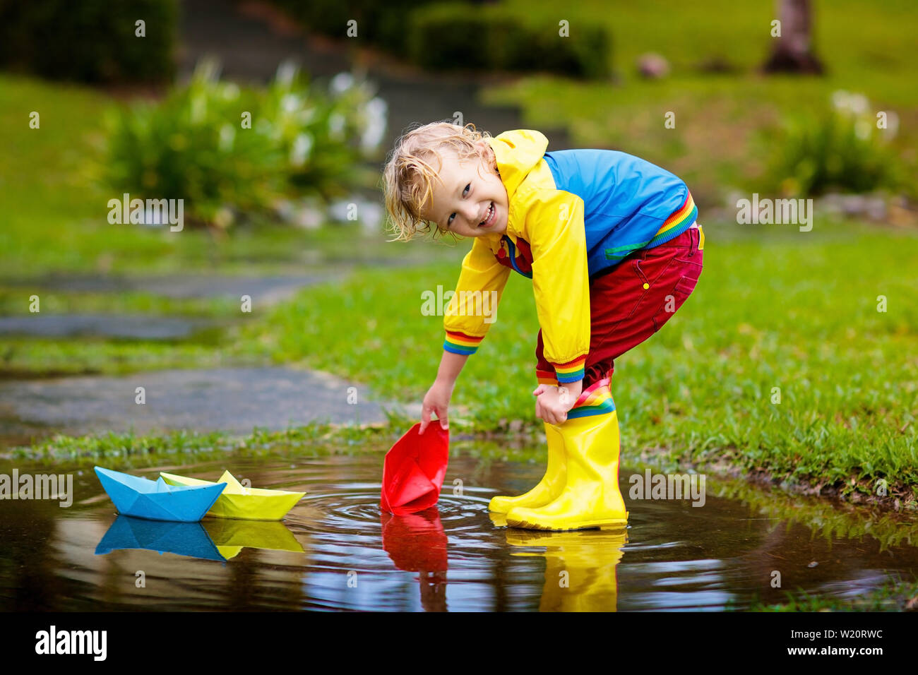 Child playing with paper boat in puddle. Kids play outdoor by ...