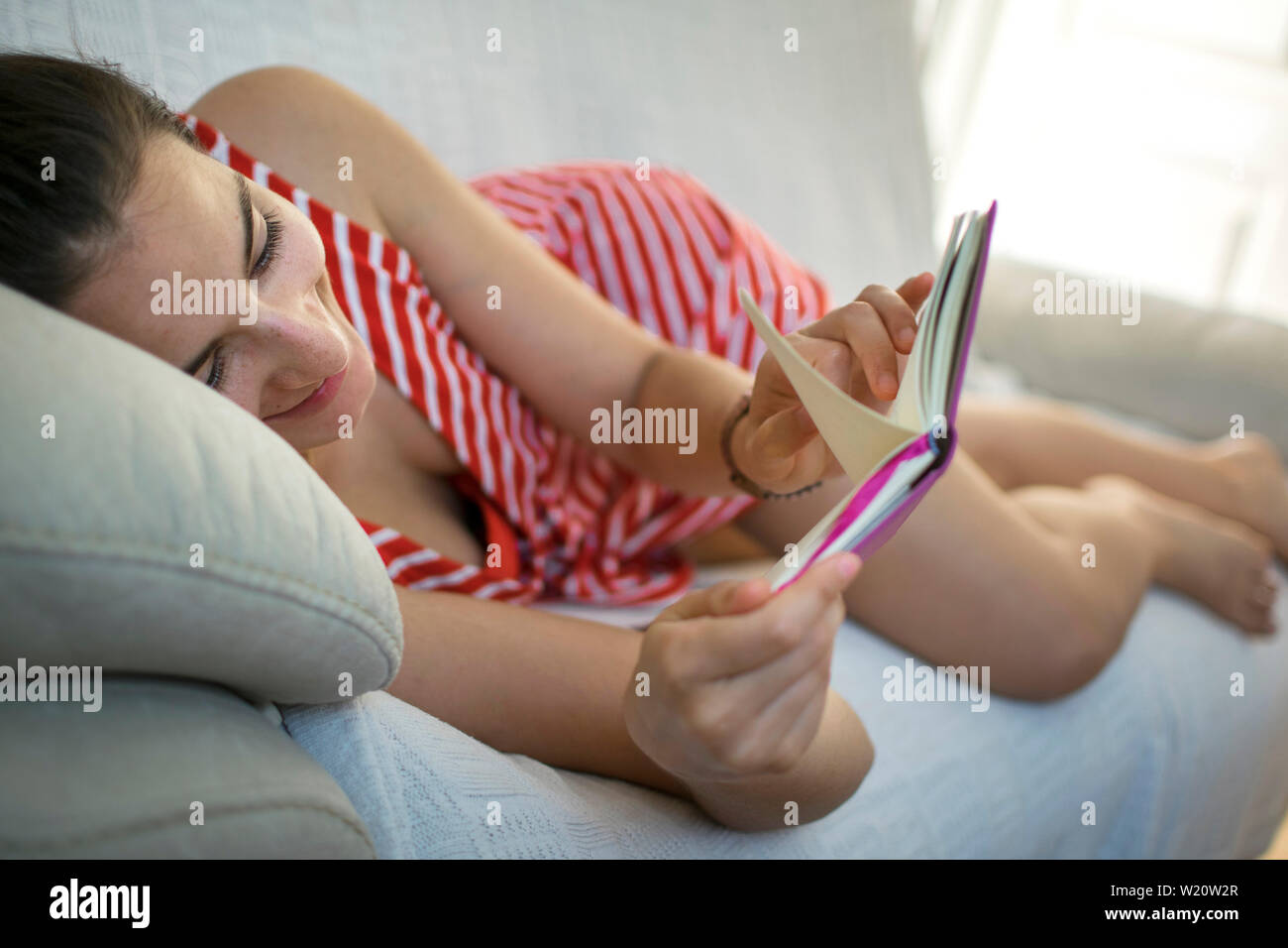 Girl Lying On The Couch Reading A Funny Book In Summer A Young