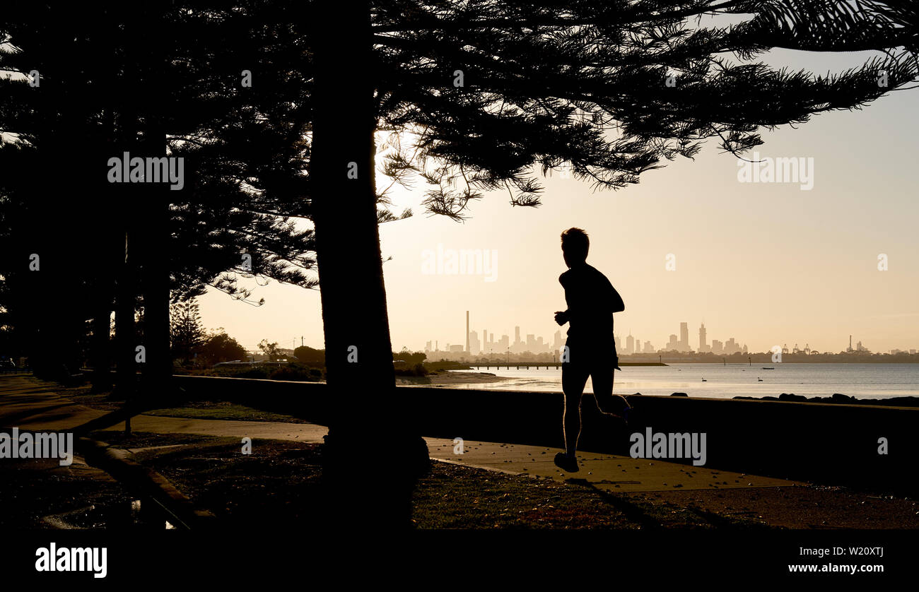 Early morning jogger silhouetted against the skyline of the distance city of Melbourne, Australia. Stock Photo