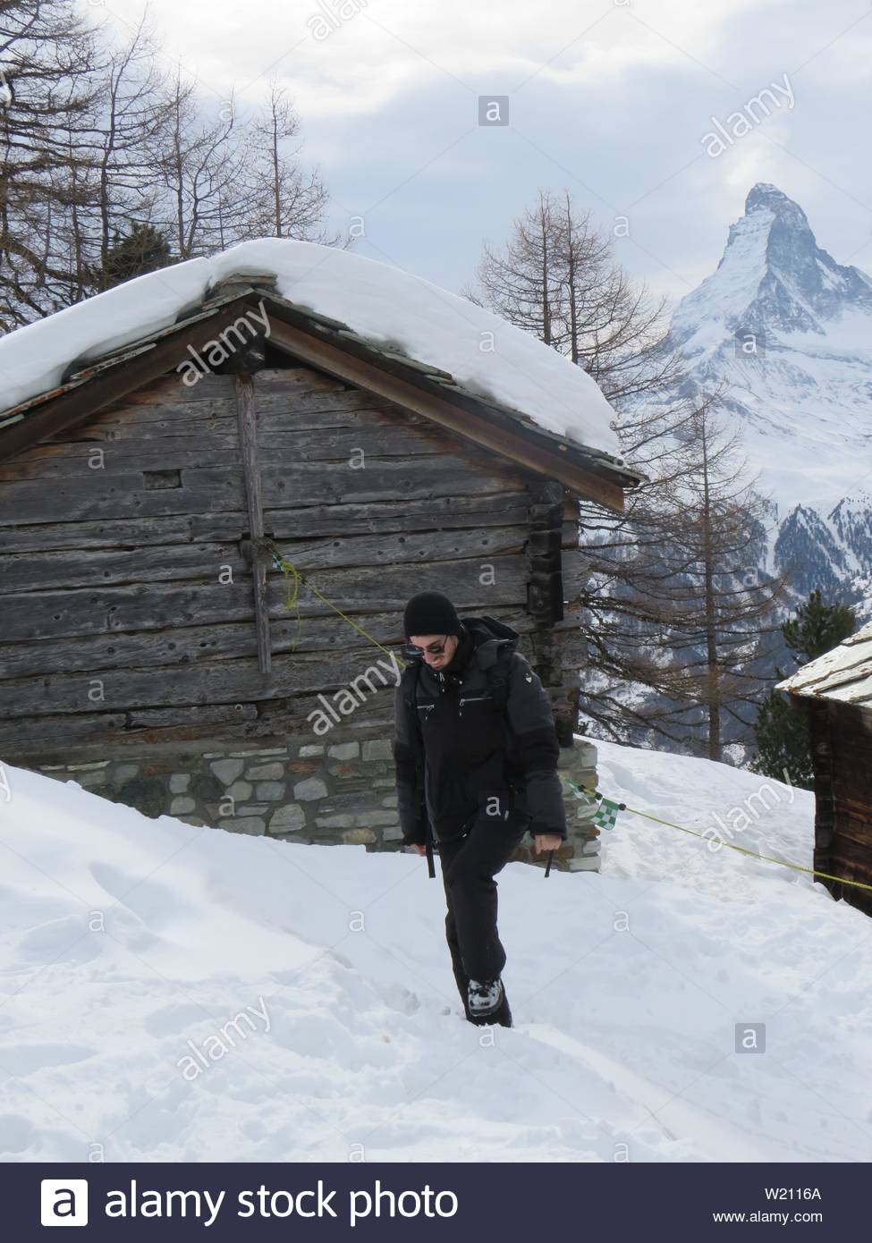 A Bundled Up Person Stands In The Snow Outside Some Cabins Stock