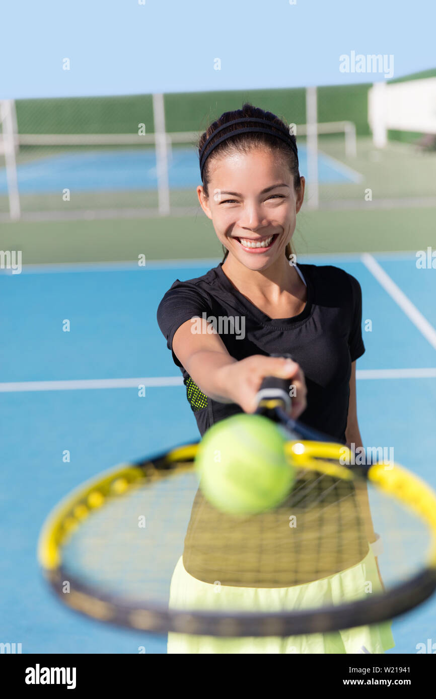 Tennis girl holding racket and ball on court. Asian woman sport athlete showing sports equipment on outdoor summer club for fitness workout. Attractive ethnic person smiling. Stock Photo