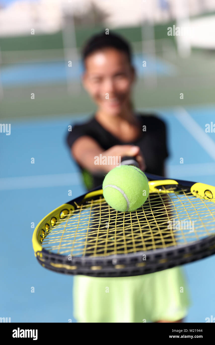 Tennis player woman showing ball on racquet / tennis racket. Unrecognizable female athlete holding fitness equipment - closeup of yellow ball on outdoor summer court. Sport activity. Stock Photo