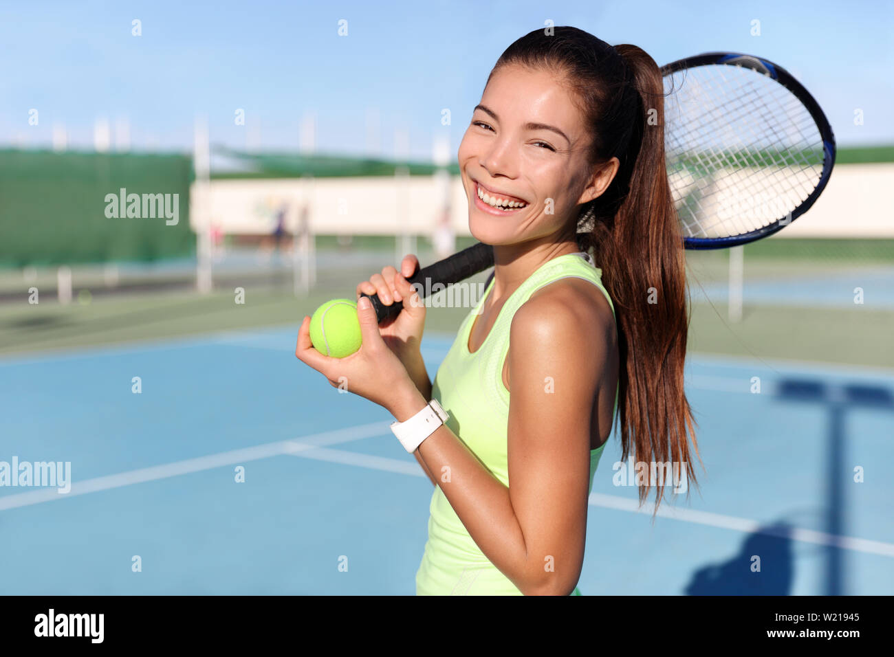 Happy tennis player girl holding racquet / tennis racket and ball on outdoor court portrait. Asian young woman fitness trainer ready for playing game match during summer. Sports activity. Stock Photo