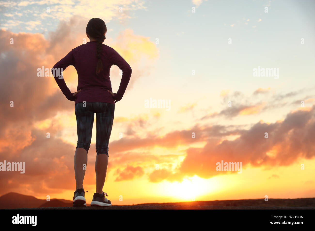 Active woman looking ahead at sunset sky for life challenge. Runner athlete getting ready for trail run thinking goal achievement choice and happiness. Female sports person living healthy lifestyle. Stock Photo