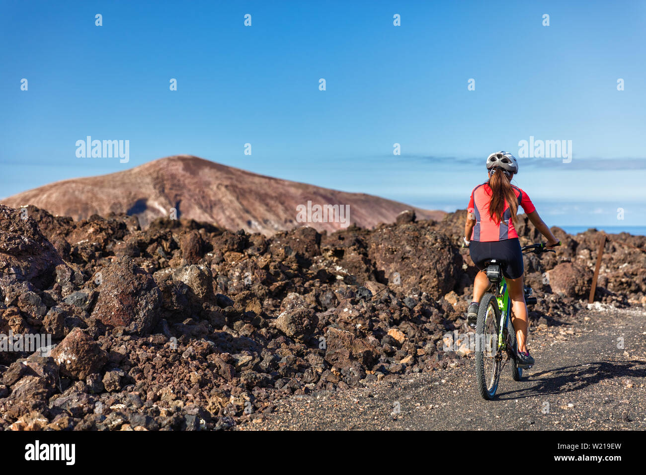 Mountain biking woman MTB cyclist cycling on nature volcano volcanic trail on vacation travel against mountains. Tourist doing sports activity during summer holidays. Leisure tourism, ecotourism. Stock Photo