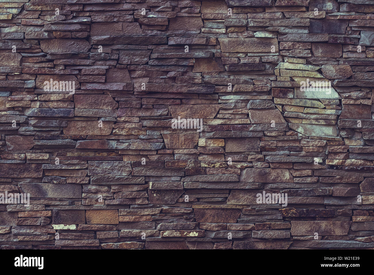 Old brick wall background. Dark brown rough stone wall. Rock wall surface. Stony texture. Grunge material background. Pattern of decorative tile. Ston Stock Photo