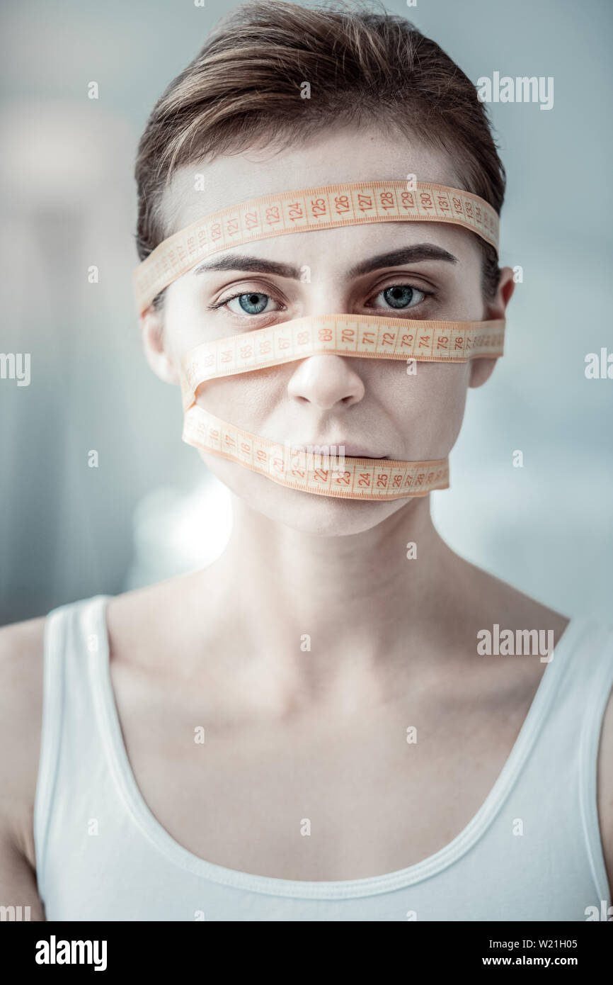 Creative model. Serious woman having measuring tape on face while posing on camera Stock Photo