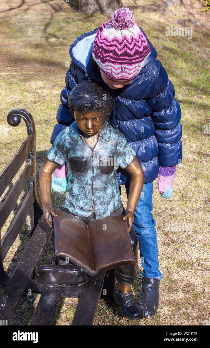 Young Girl Looking Over Shoulder Of Statue Of Child On Park Bench