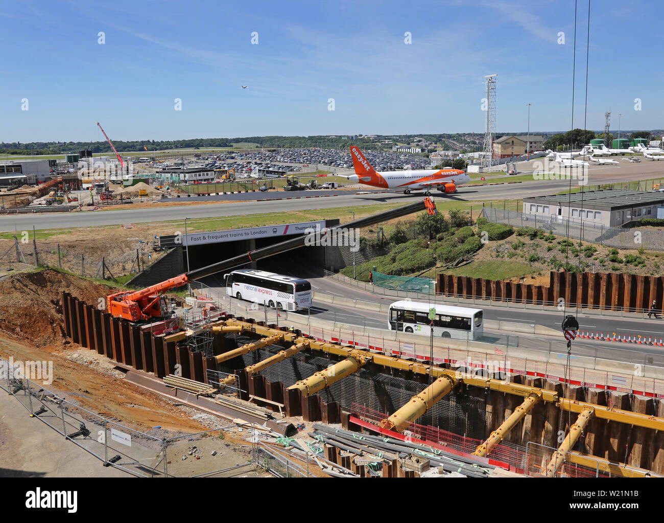 London Luton Airport, UK. Excavation for the new DART rail link. Also shows main access road beneath airport taxiway with Easyjet plane passing. Stock Photo