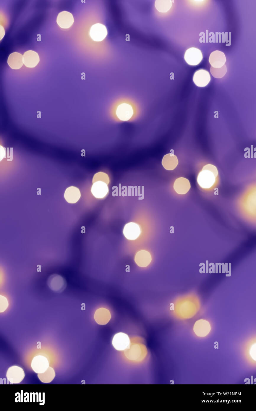 Golden festive bokeh lights on blurred violet background. Christmas or party concept. Stock Photo