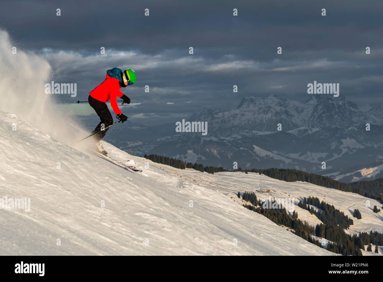 Female skier skiing steep downhill, black piste, behind mountains, Brixen im Thale, Tyrol, Austria Stock Photo