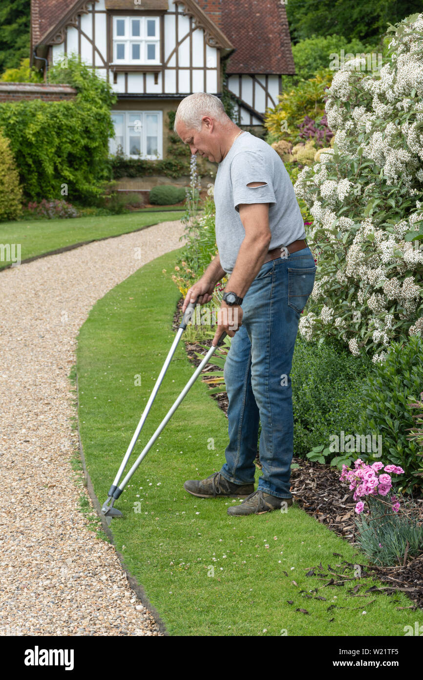Gardener trimming or edging a formal lawn with long-handled lawn-edging shears Stock Photo