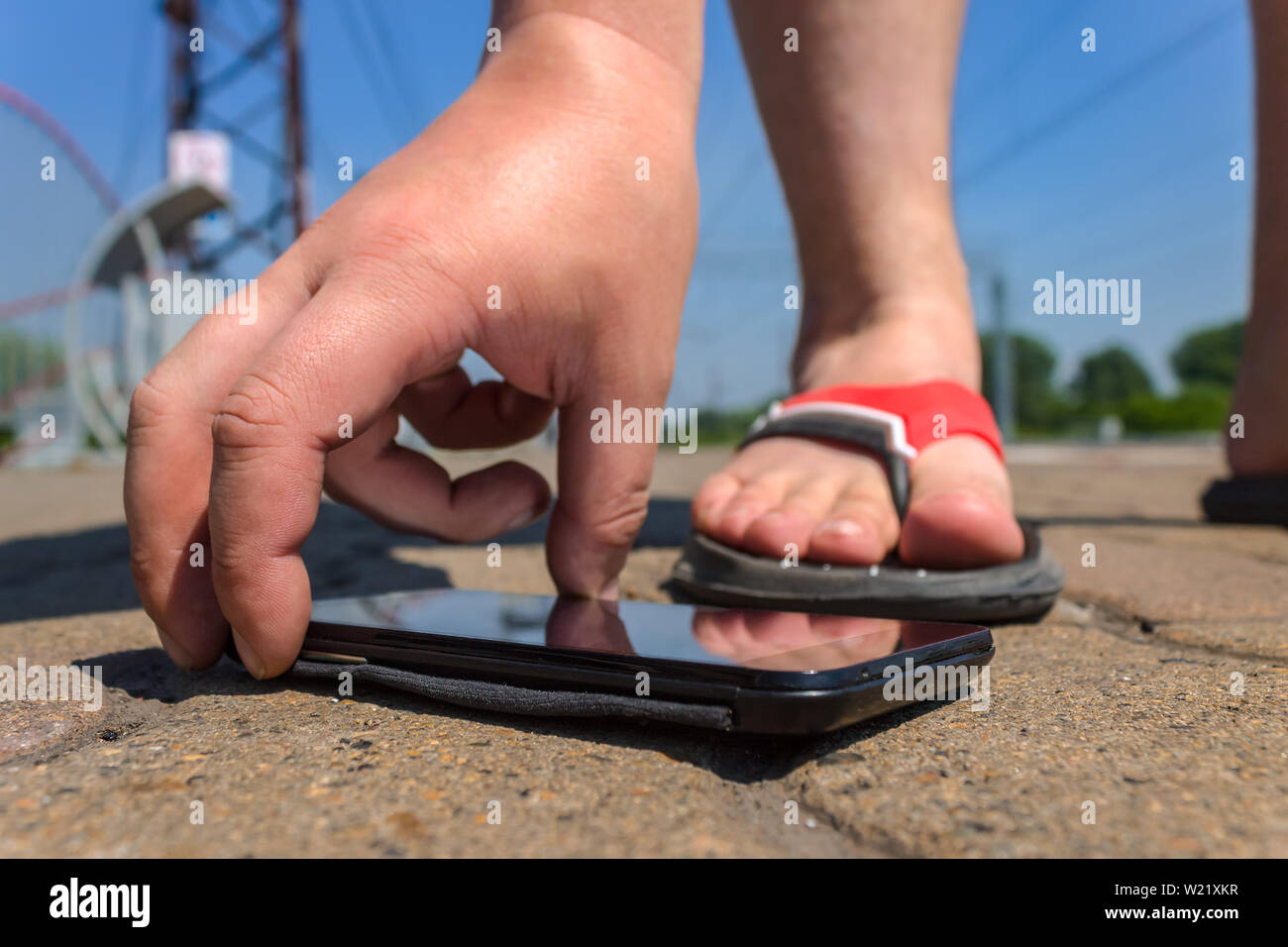 A man lifts a smartphone in a public park fallen on the road Stock Photo