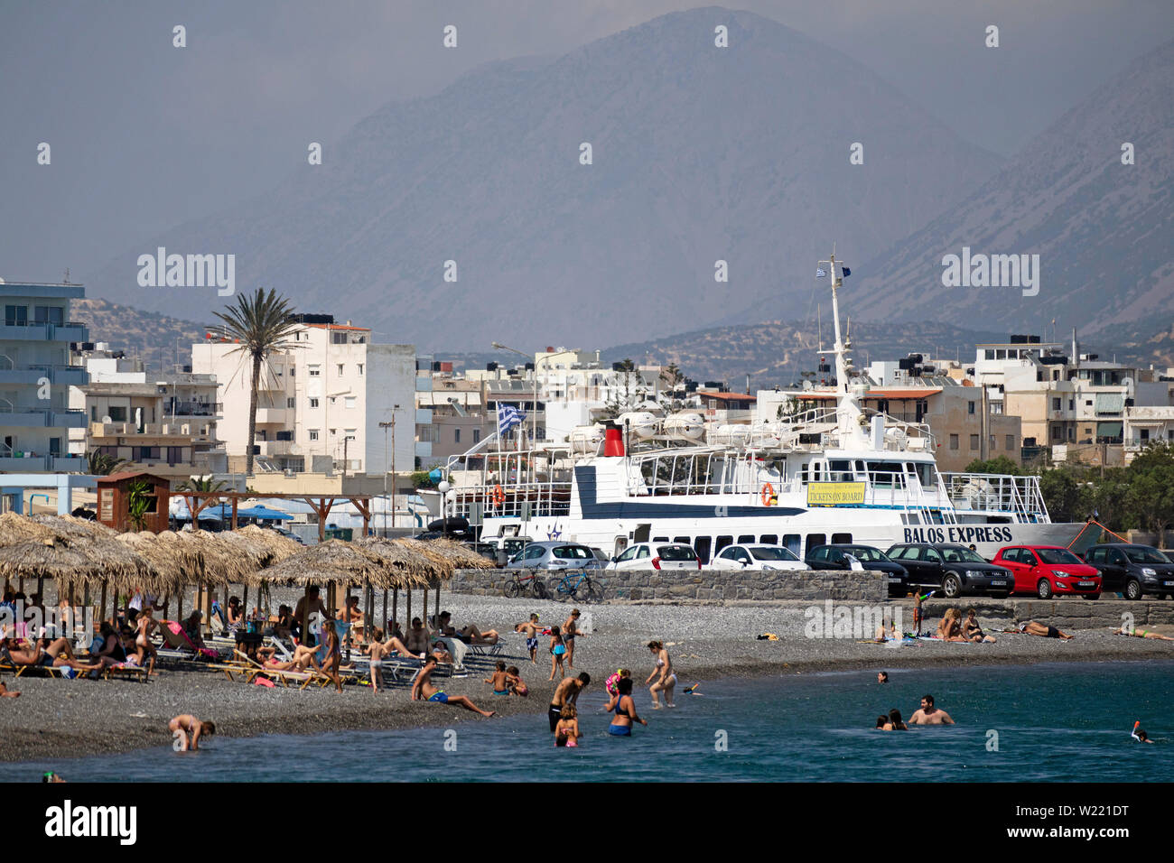 Ierapetra, Crete, Greece. June 2019. The southern coastal town of Ierapetra with holidaymakers on the beach and a Chrissi Island ferry in port. Stock Photo