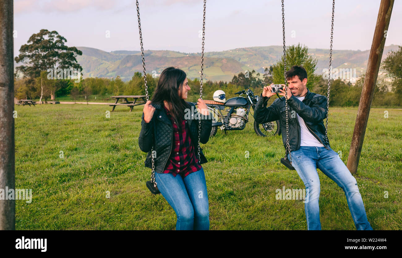 Young man taking a picture of his girlfriend on the swings Stock Photo