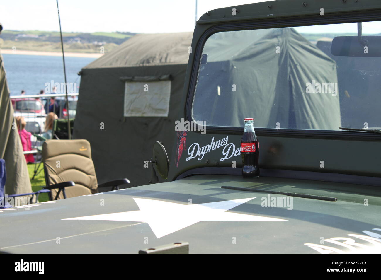 A glass CocaCola bottle sits on the bonnet of a US Army Jeep beside a label saying Daphnes Devil seen at Portrush Air Waves 2019 Stock Photo