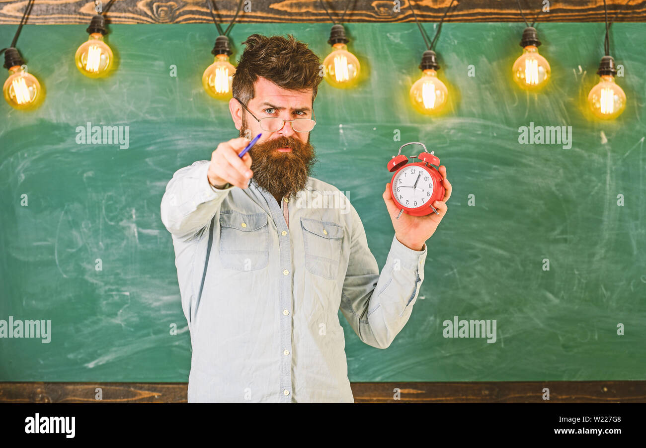 Bearded hipster holds clock, chalkboard on background, copy space ...
