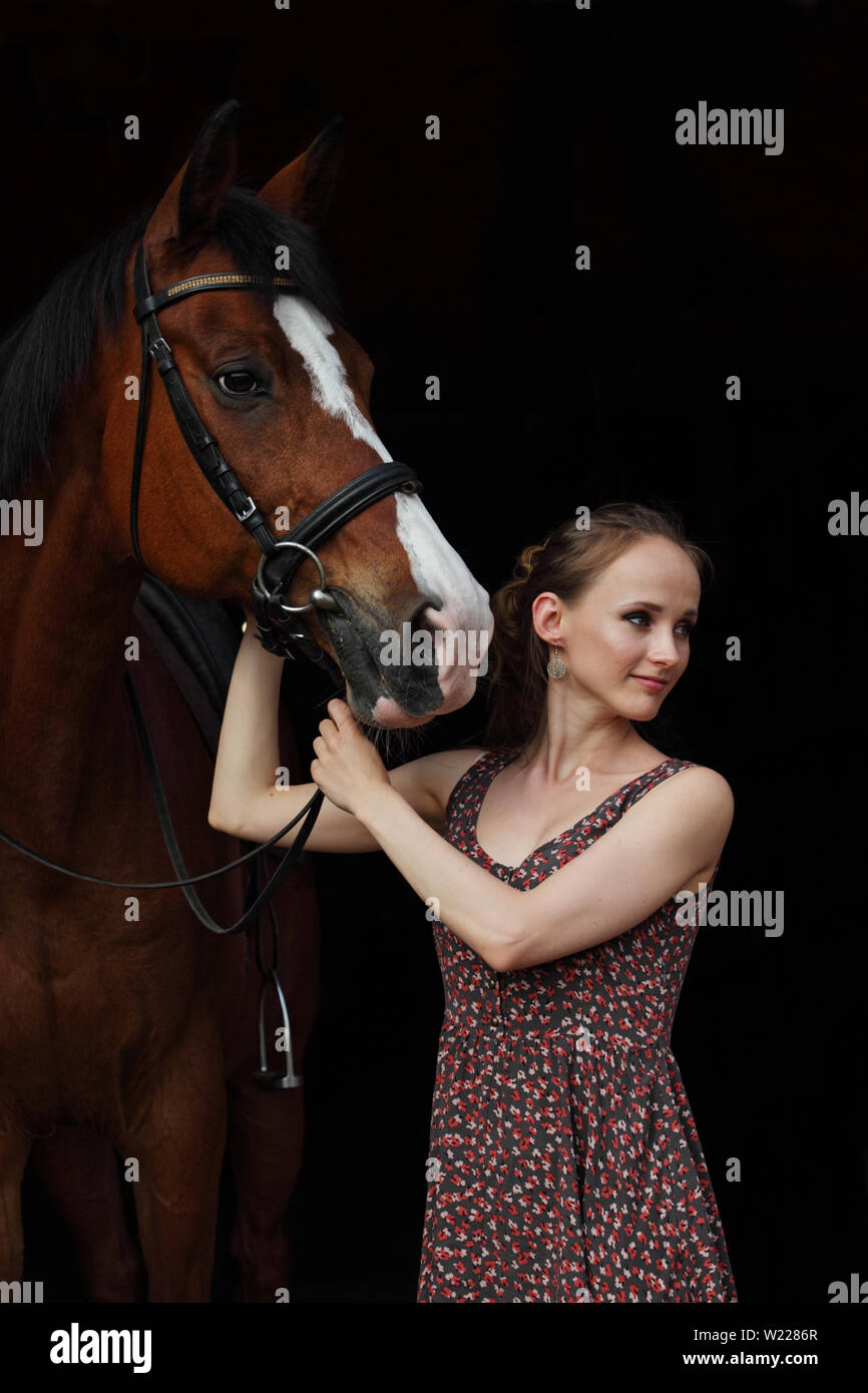 Country girl leads a horse out of the dark stable, low key portrait Stock Photo