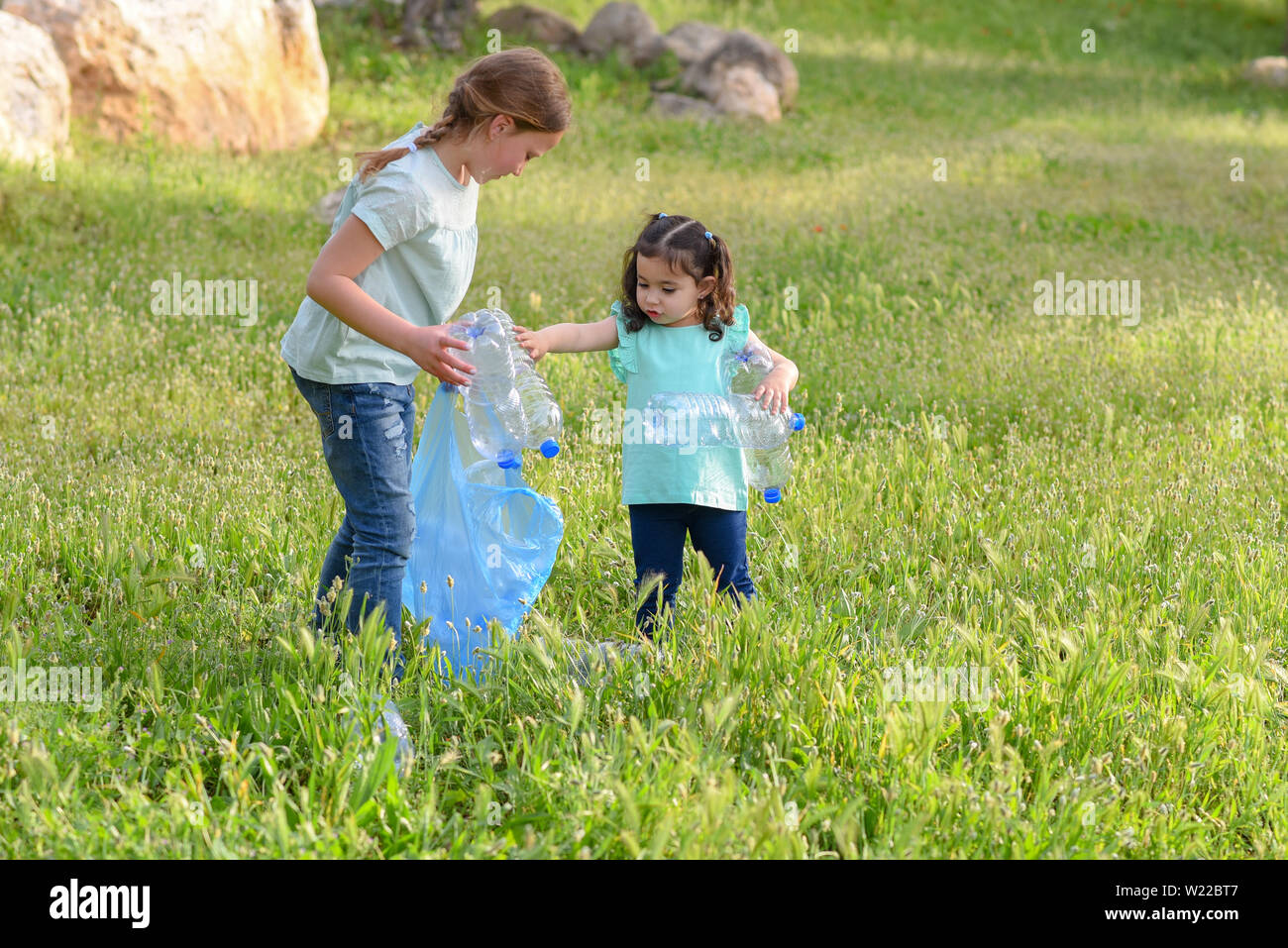 Cute little girls cleaning up plastic litter on grass. Children