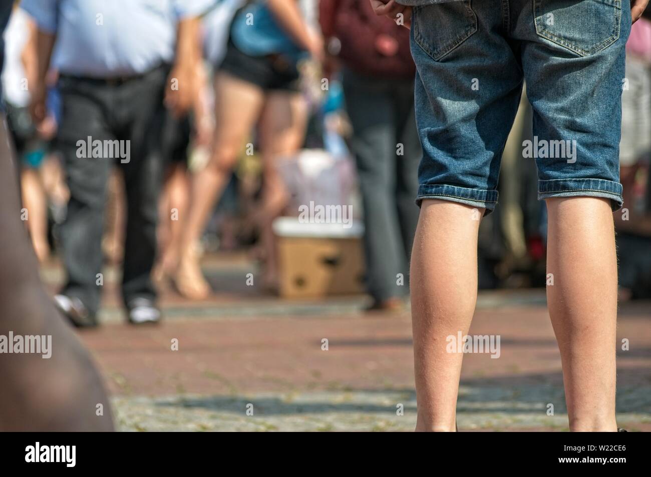 single woman standing before a crowd of people at a weekend flea market on the streets with blurred background Stock Photo