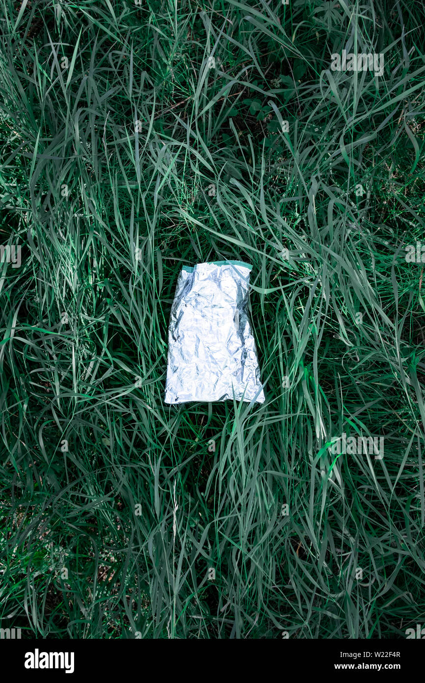 Plastic bag in green grass, nature pollution concept. Piece of plastic trash (empty food package) thrown away on a lawn Stock Photo