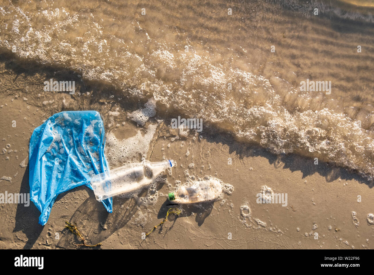 Plastic bag and bottles on the beach, seashore and water pollution concept. Trash (empty food package) thrown away at the seaside, top view with waves Stock Photo