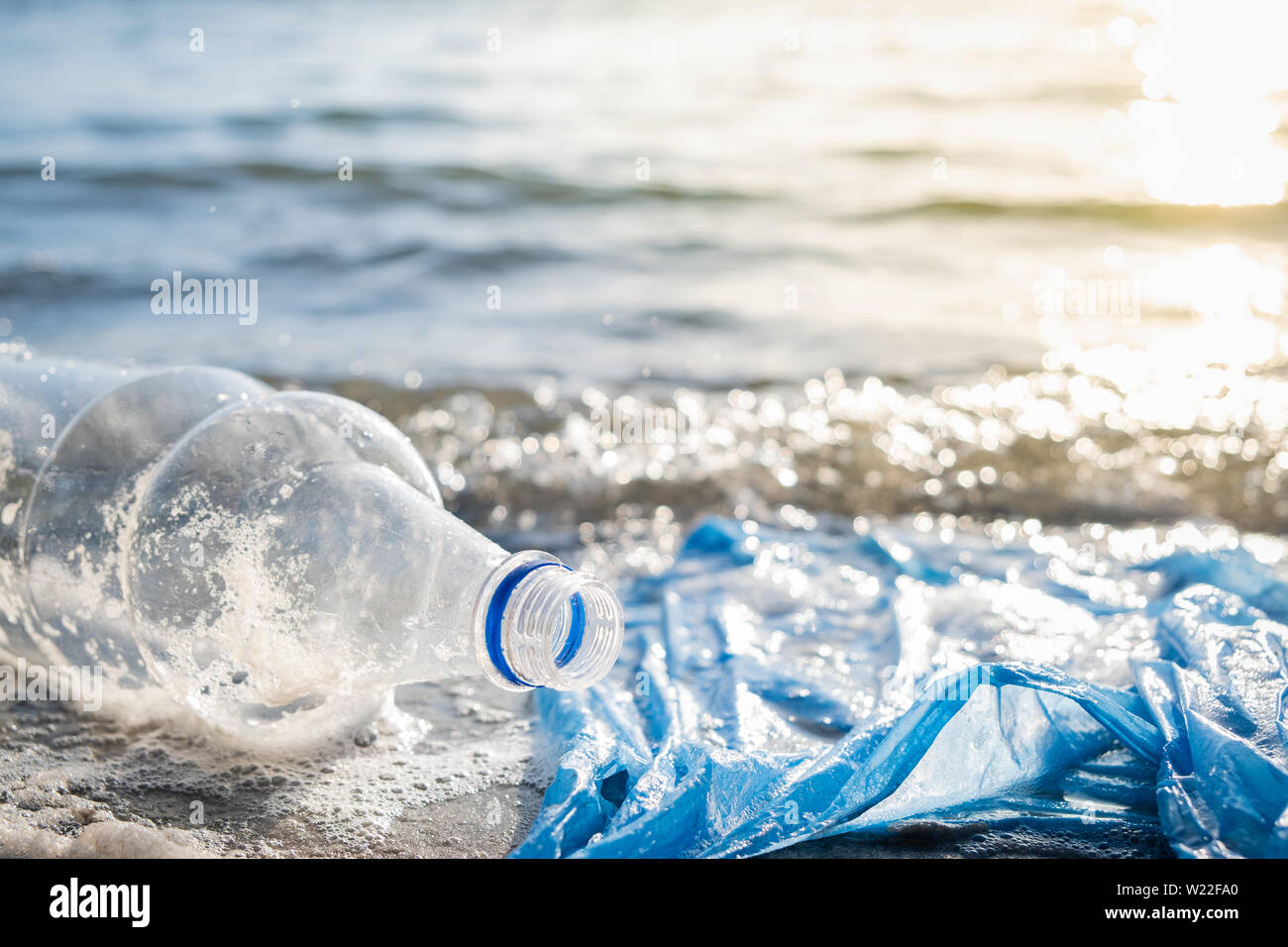 Plastic bag and bottles on the beach, seashore and water pollution concept. Trash (empty food package) thrown away at the seaside, close-up view in di Stock Photo