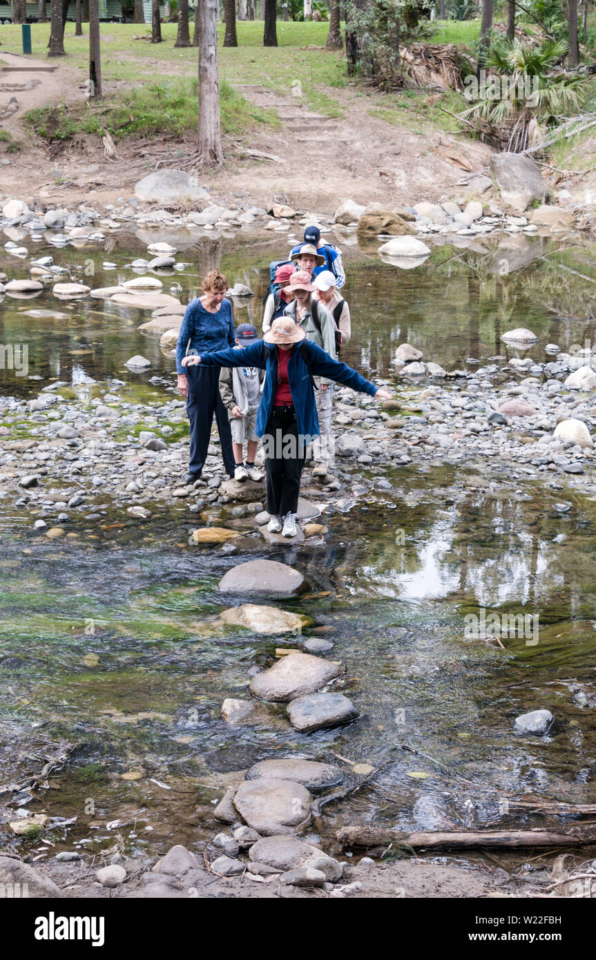 A group of Australian hikers crossing over a row of stepping stones across the Carnarvon Creek within the Carnarvon Gorge National Park in the Central Stock Photo