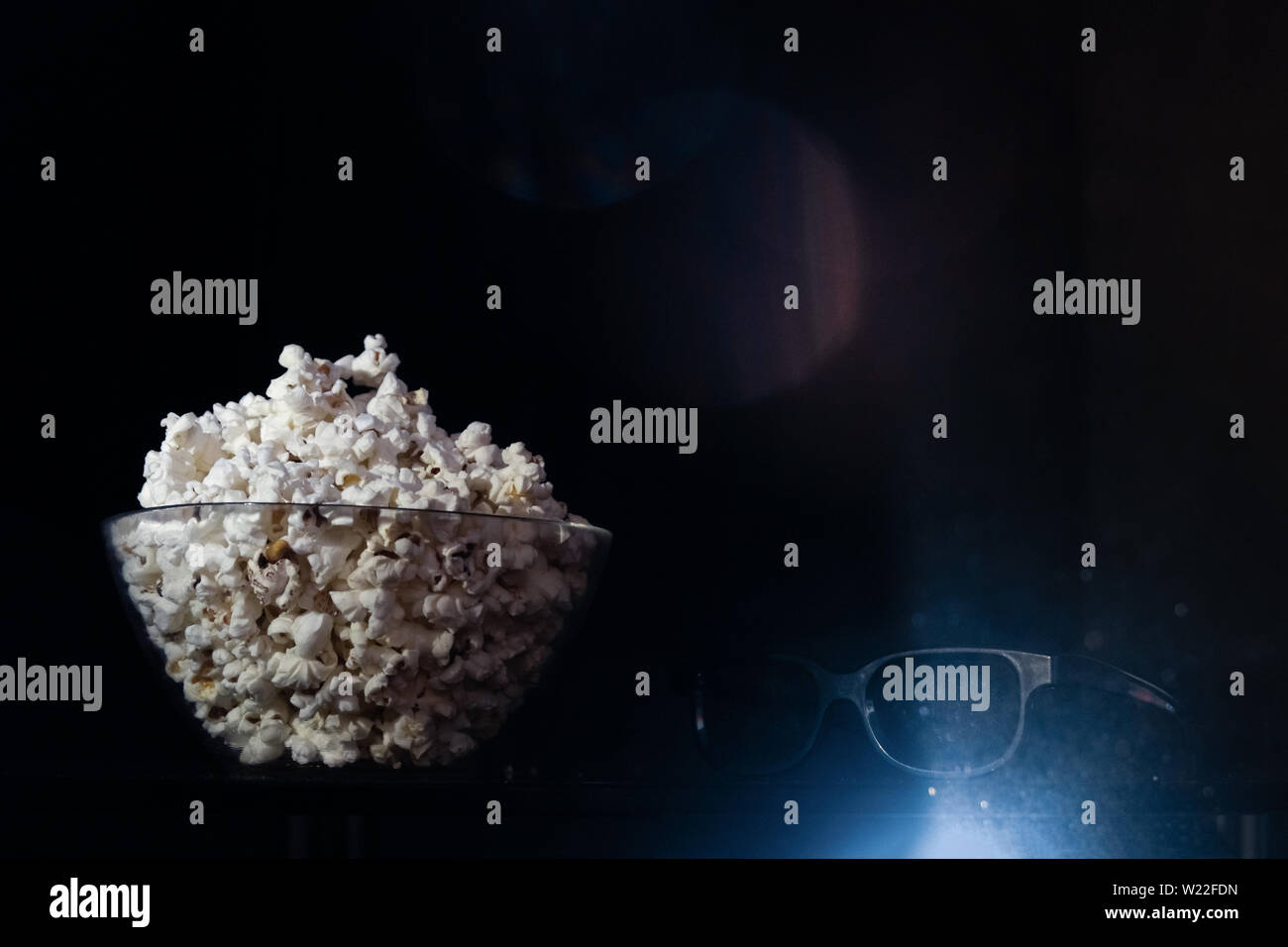 Bowl of popcorn and 3d cinema glasses in black background. Cinema, 3d movies watching conceptL snacks and 3d goggles and bright flare of light from a Stock Photo