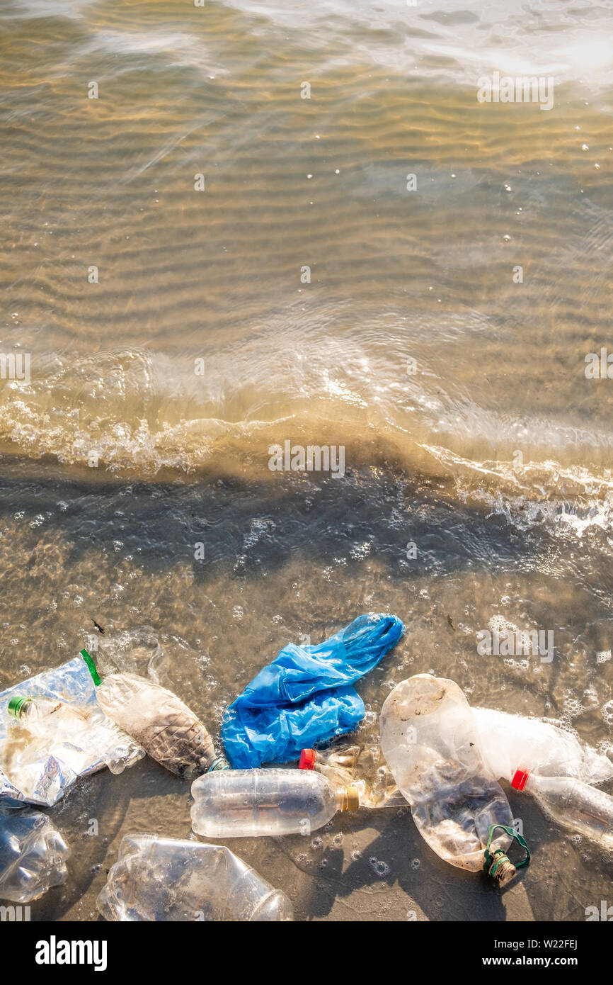 Plastic bag and bottles on the beach, seashore and water pollution concept. Trash (empty food package) thrown away at the seaside, top view with waves Stock Photo