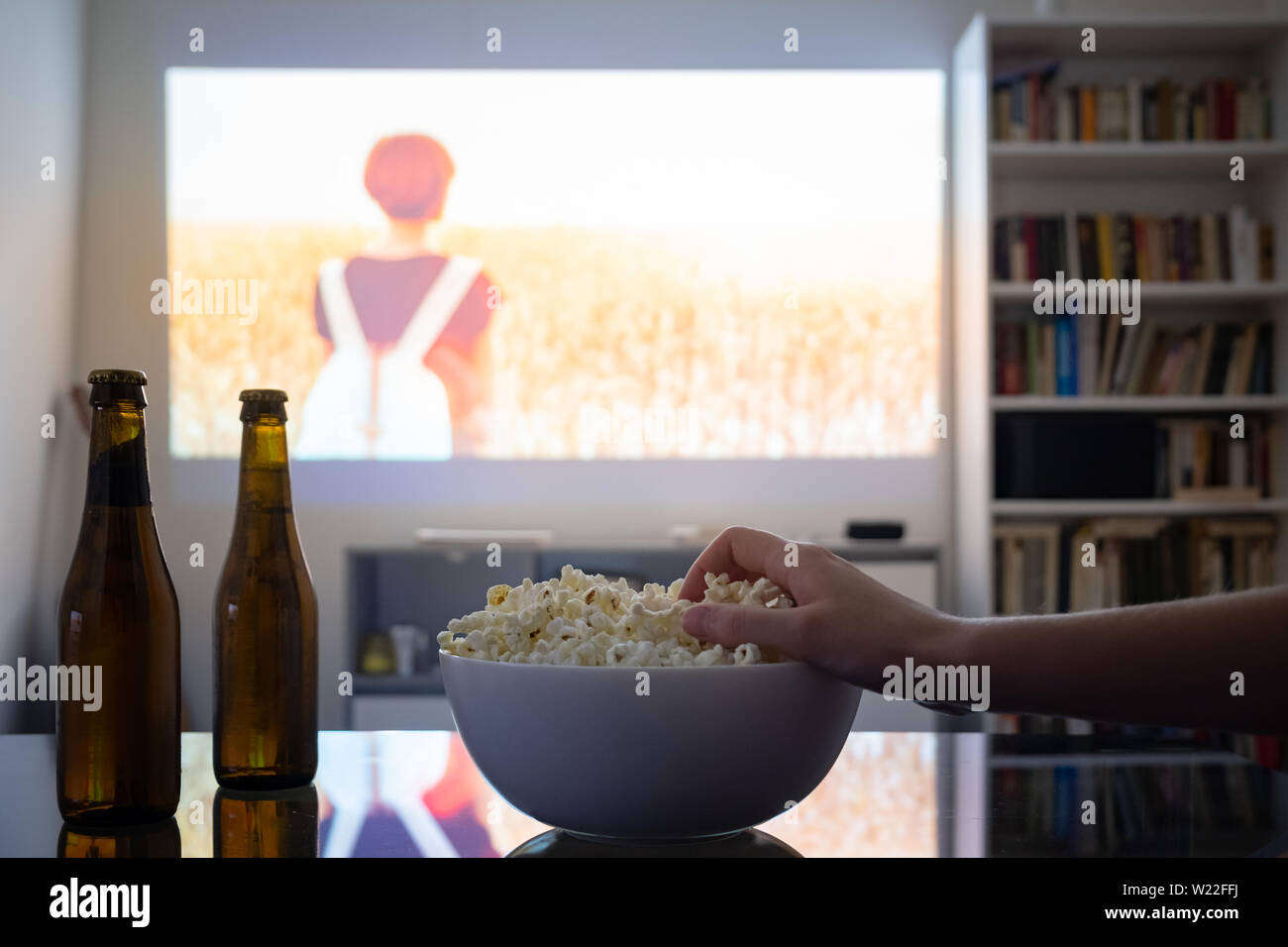 Home cinema entertainment: watching a film from a video projector in a room. Dim living room with a cinematic picture projected on the wall, human han Stock Photo