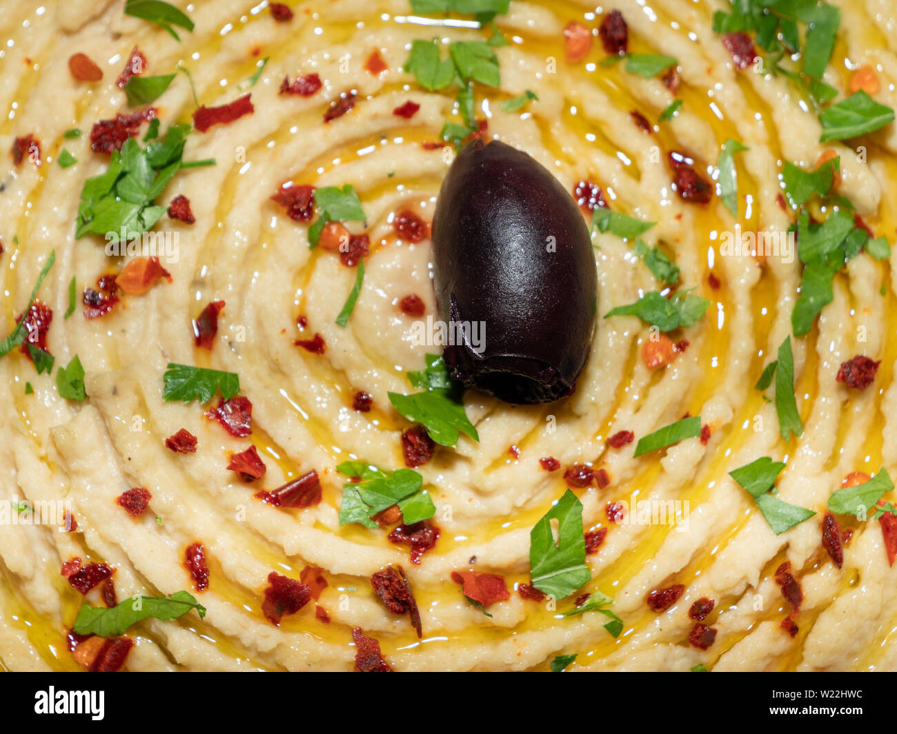 Hummus garnished with Olive, Pepper Flakes and Chopped Parsley. Oriental, Turkish appetizer or starter called meze. Stock Photo