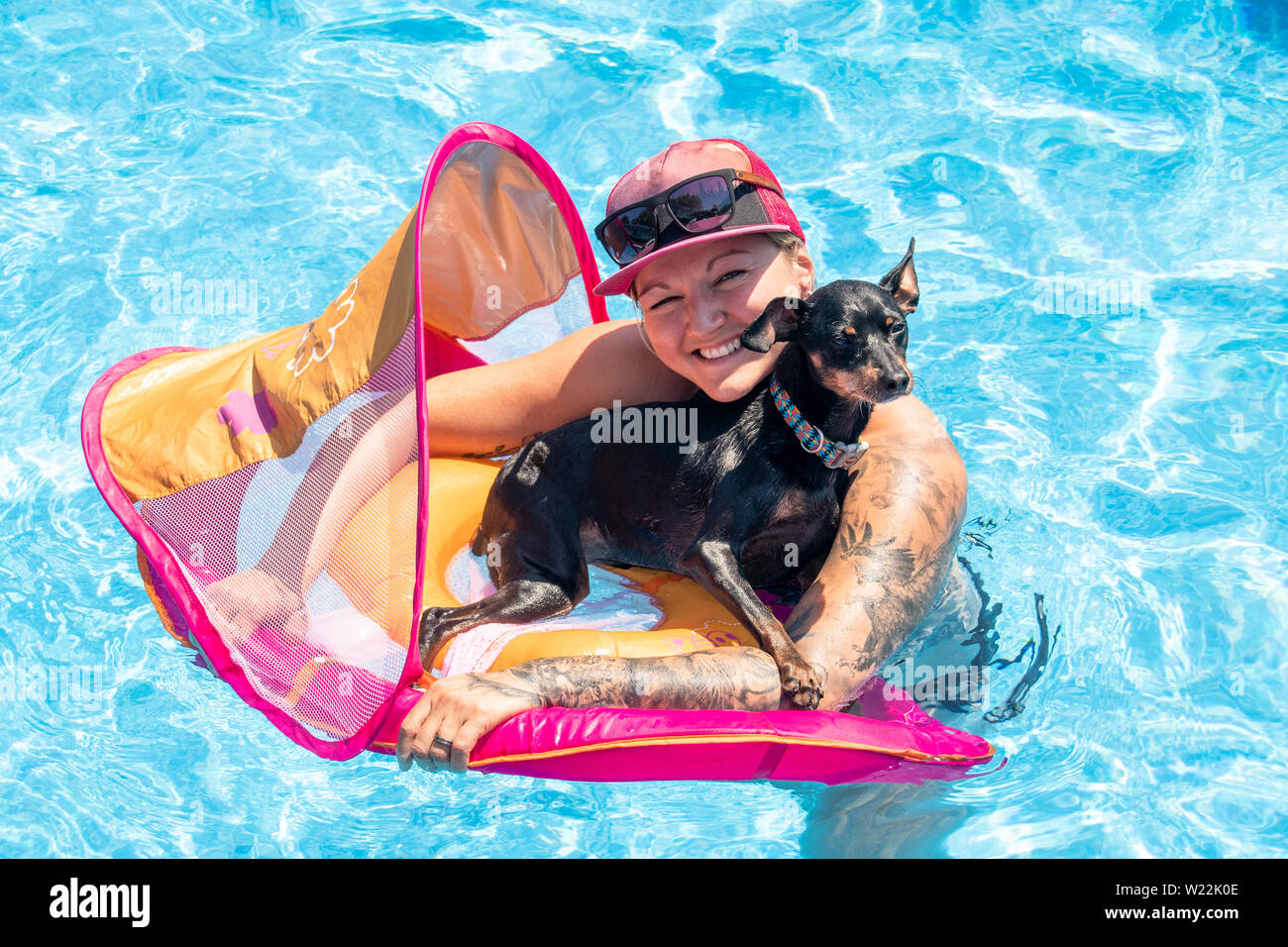 caucasian woman relaxing with black pinscher dog on a flotation device in the swimming pool Stock Photo