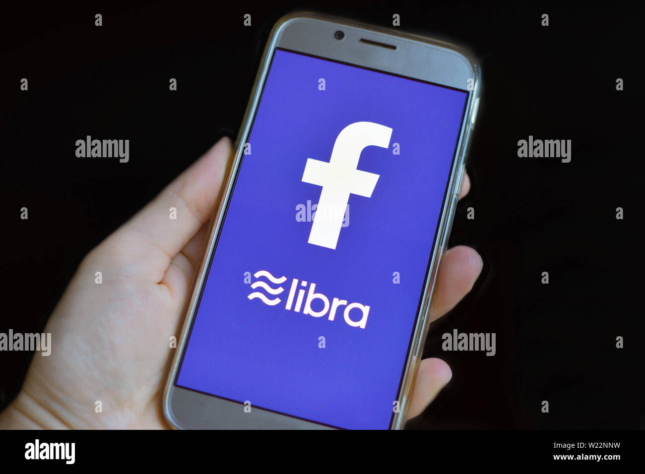 Cryptocurrency Libra concept with hand holding cellphone with Libra and Facebook logo on bue mobile phone Stock Photo