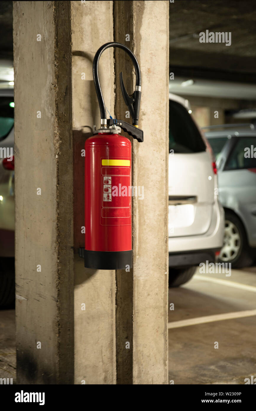 Fire extinguisher hung on a wall in a car park with cars Stock Photo